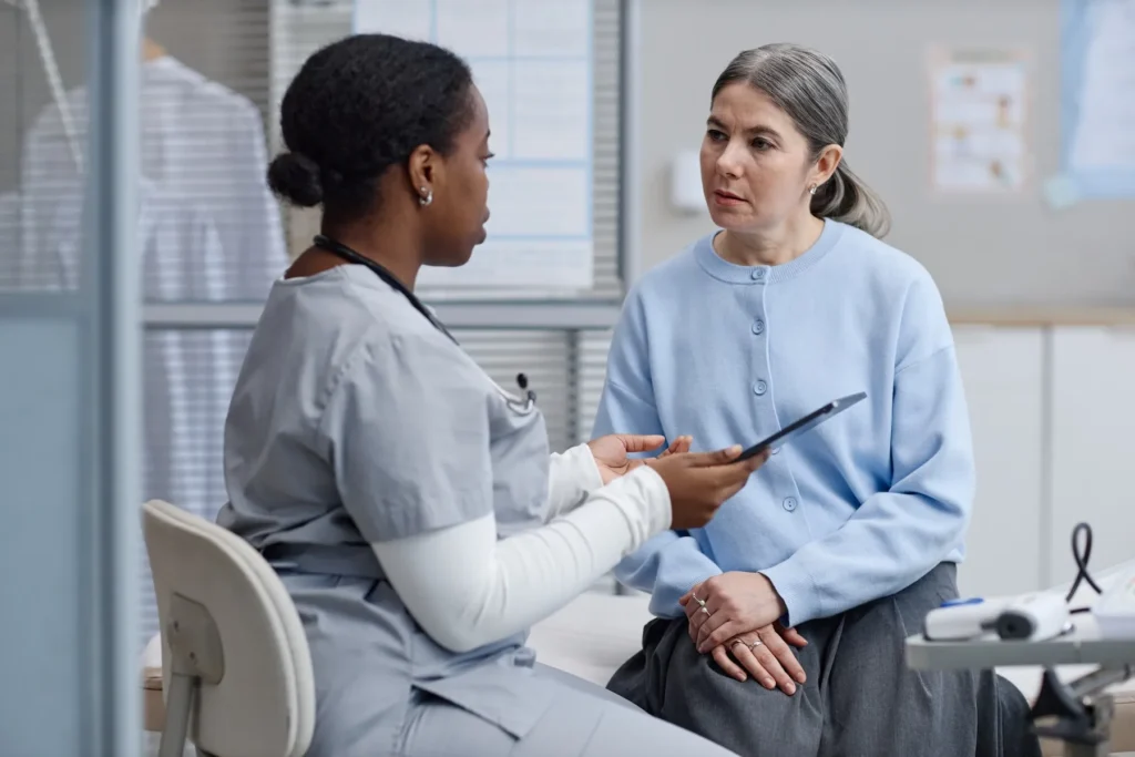 A healthcare worker in scrubs talks with a woman about breast reconstruction.