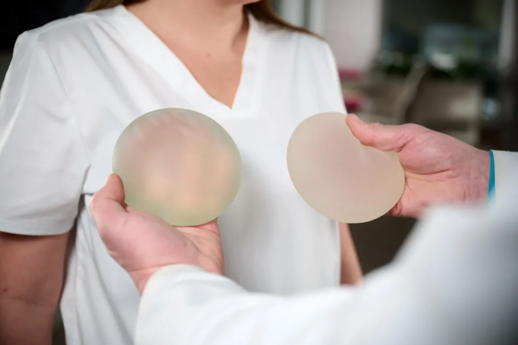 Two people in lab coats examine silicone breast implants together in a clinical setting, discussing reconstruction options.