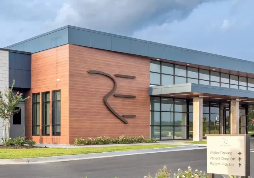 ReCenter specialized breast cancer hospital exterior, a Contemporary building with wood and glass accents, a prominent "RE" logo, and a sign for ReCenter breast cancer hospital.