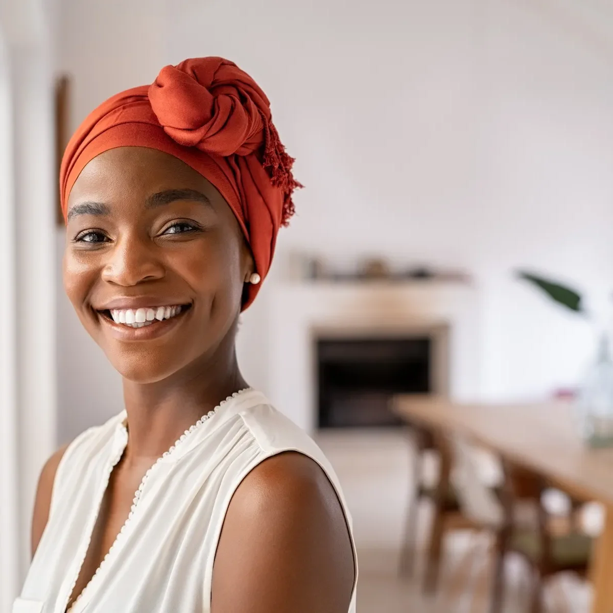 A smiling woman wearing an orange headwrap with an apex flap in a home interior.