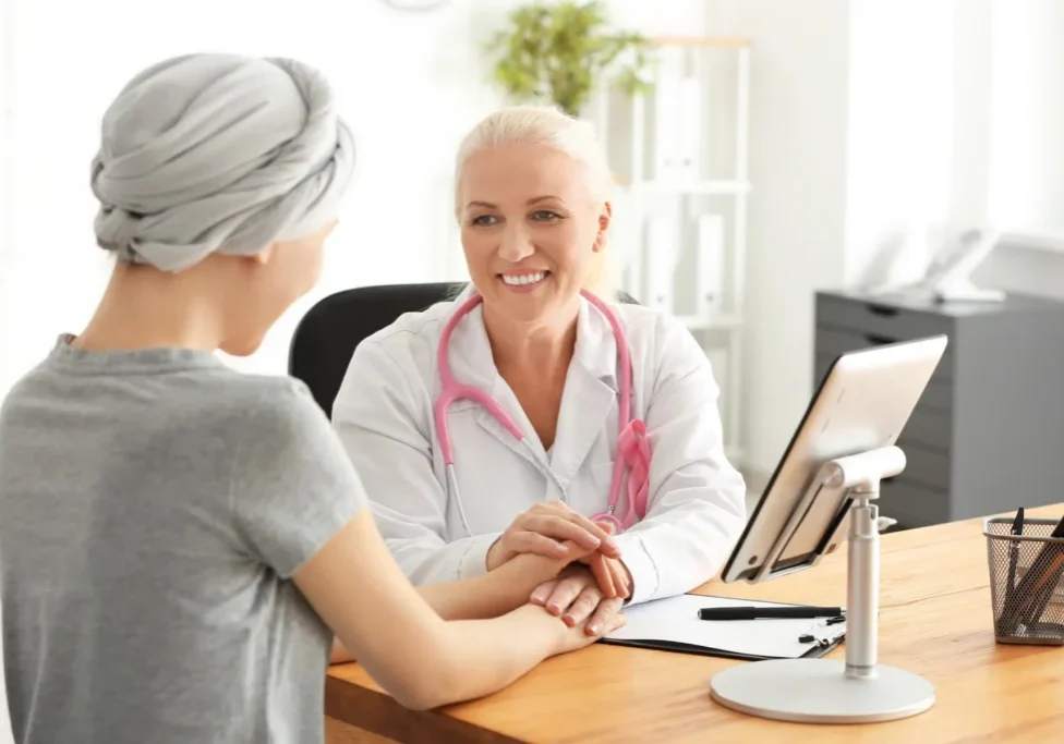 A smiling doctor with a pink stethoscope holds hands with a headscarf-wearing patient at ReCenter.